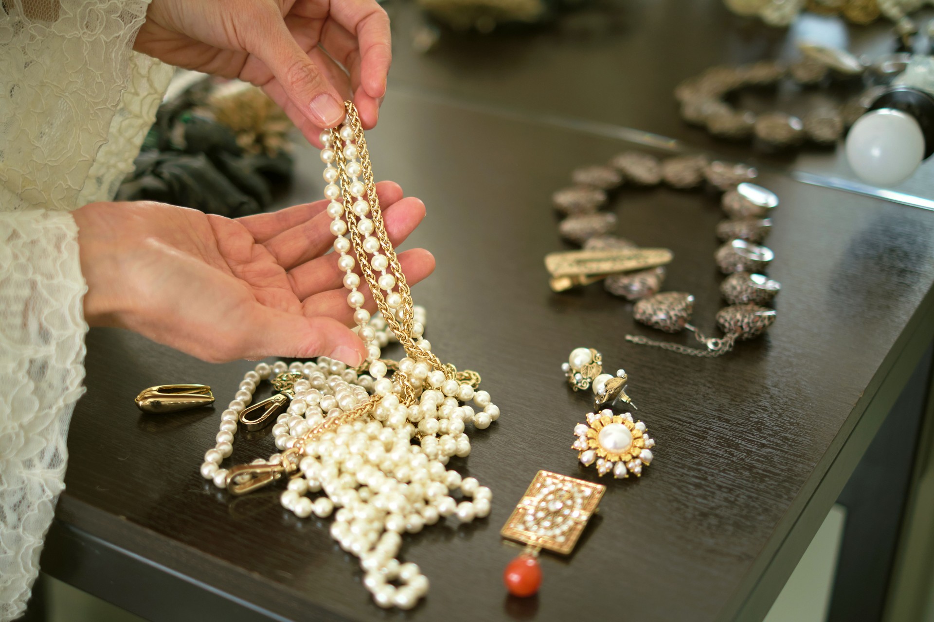 A person holds a pearl necklace over a table filled with various pieces of jewelry. This image showcases the elegance and beauty of fine accessories.